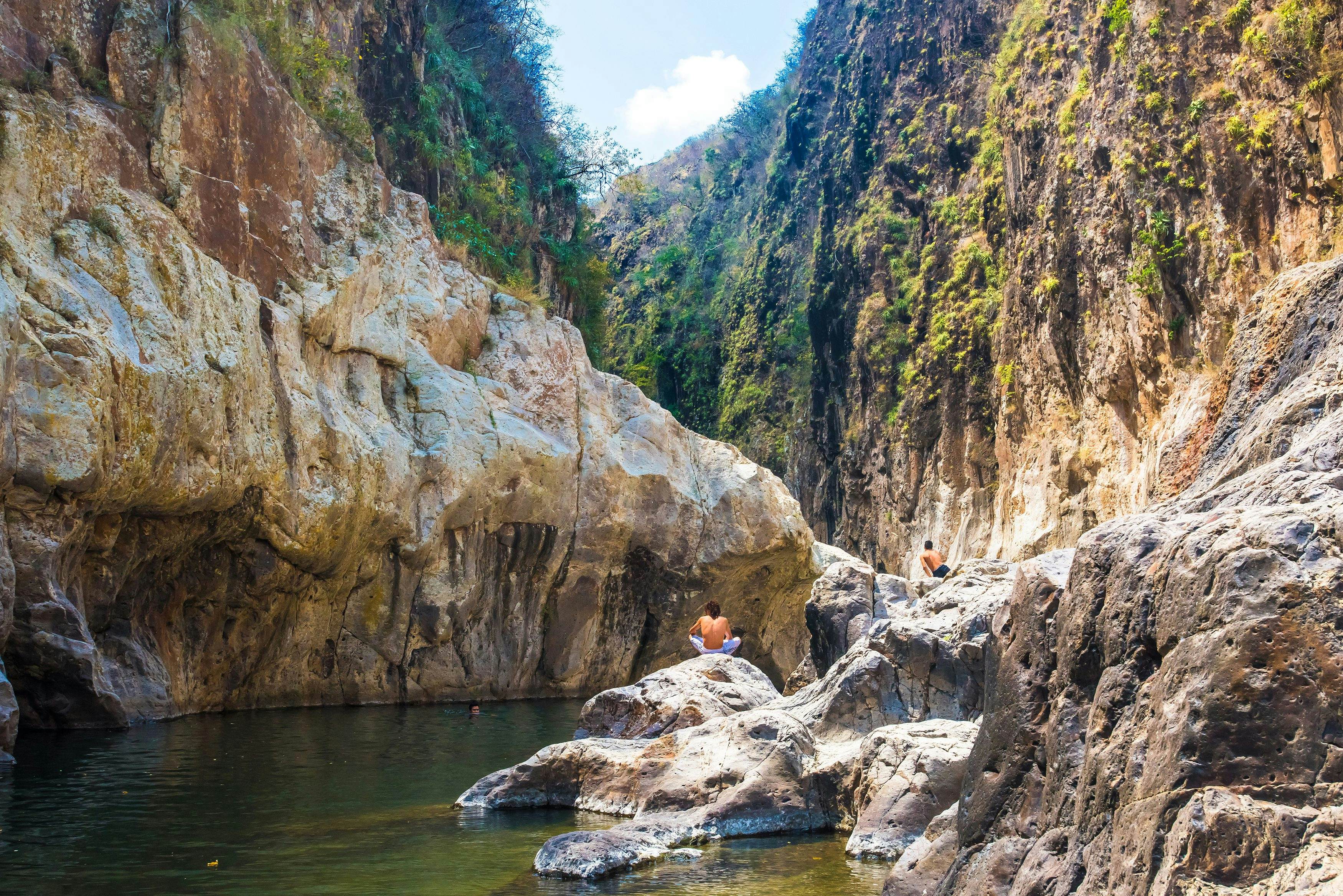 Somoto Canyon, Nicaragua. Man in the distance sitting in a stone contemplating the peaceful stream of water flowing through the rock mountains. Beautiful dry summer natural scenery.; 
Monumento Nacional Cañon de Somoto

Shutterstock ID 1822814987; your: Bridget Brown; gl: 65050; netsuite: Online Editorial; full: POI Image Update